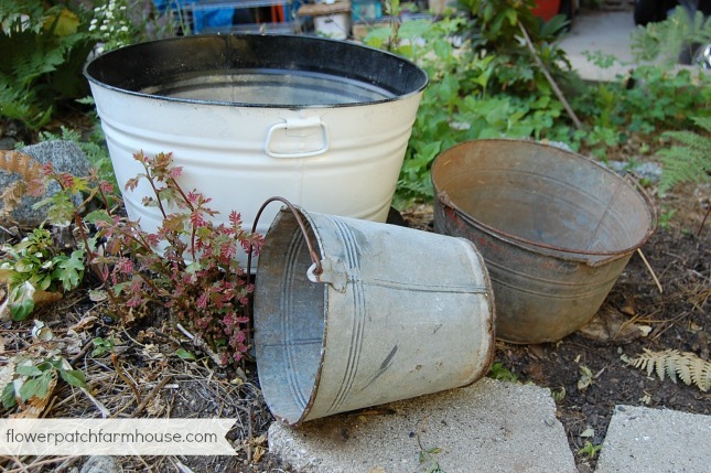 vintage buckets and galvanized tubs in the garden waiting to be planted, the larger one is painted white