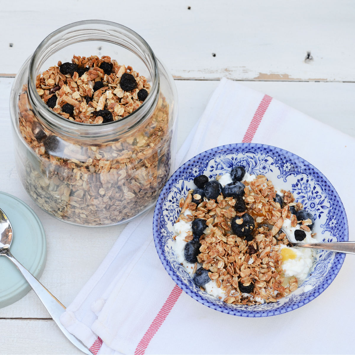 blue patterned bowl filled with granola over cottage cheese and topped with blue berries, a jar of granola sits behind