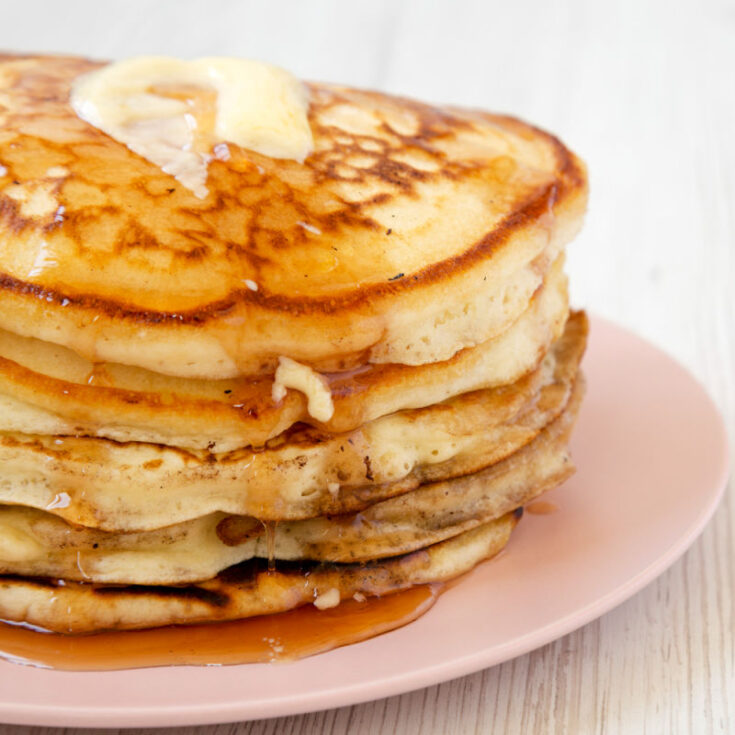 fluffy, buttered buttermilk pancakes on a plate with syrup running down edge