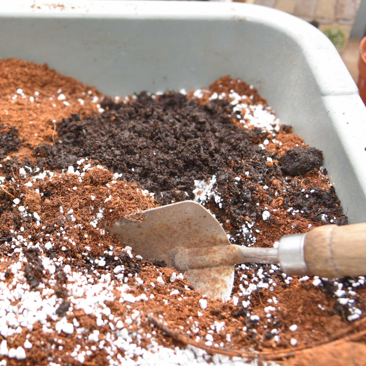 ingredients in a small tub to create DIY Pottings soil, garden trowel inserted into it