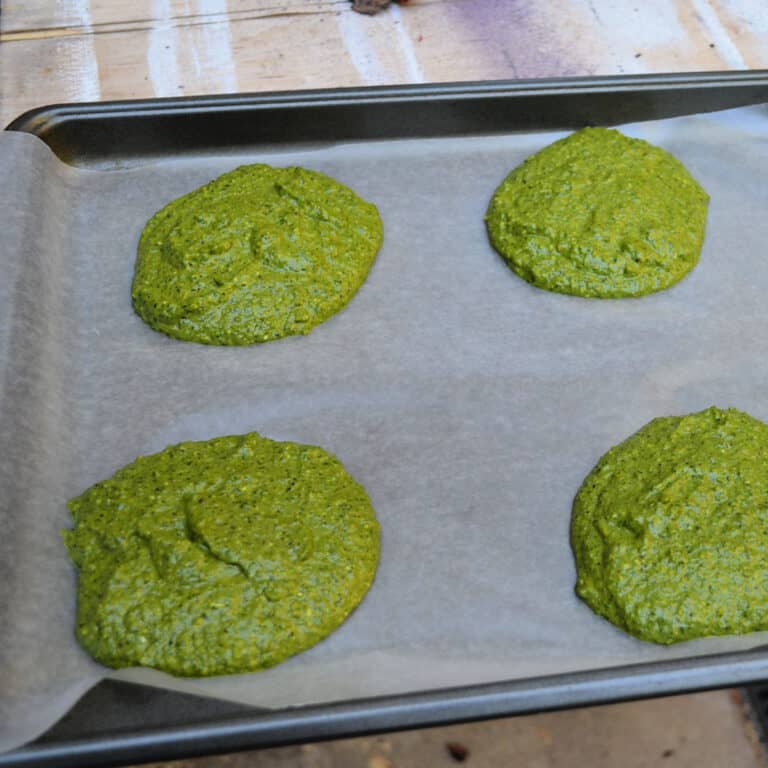 4 patties of Homemade basil pesto on a parchment covered cookie sheet