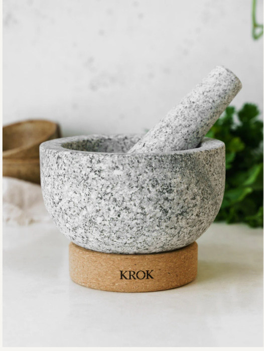 krok mortar and pestle on a white talbe with a white background and green herbs