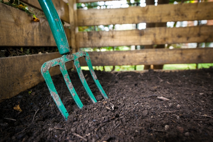 garden fork turning compost in wooden compost bin, soil health