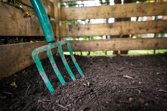 garden fork turning compost in wooden compost bin