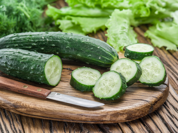 Cucumbers on the wooden cutting board with a knife.