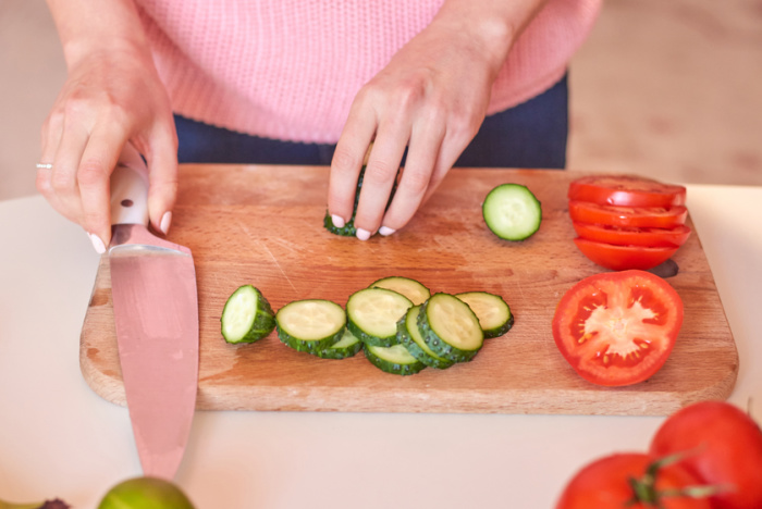 Woman hands cutting cucumbers with knife for tomato cucumber salad