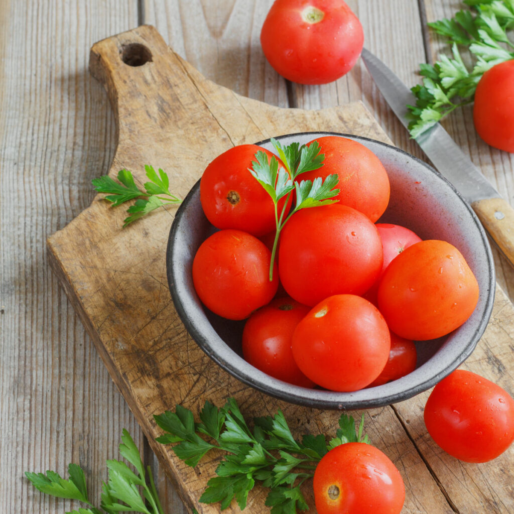 bowl of ripe tomatoes on wood cutting board with parsley