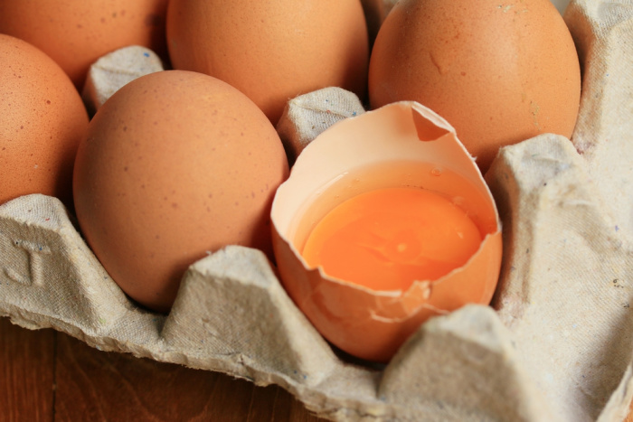 brown eggs in carton, one broken showing orange yolk