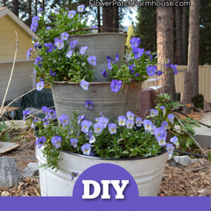 galvanized tubs stacked to create a vertical planter, planted with violas, text overlay reads: Discover How!, Flower Patch Farmhouse dot com, DIY Vertical Planter, step by step