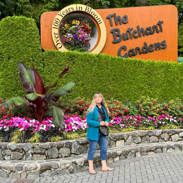 Pamela of Flower Patch standing in front of a planter with the Butchart Gardens sign in the background